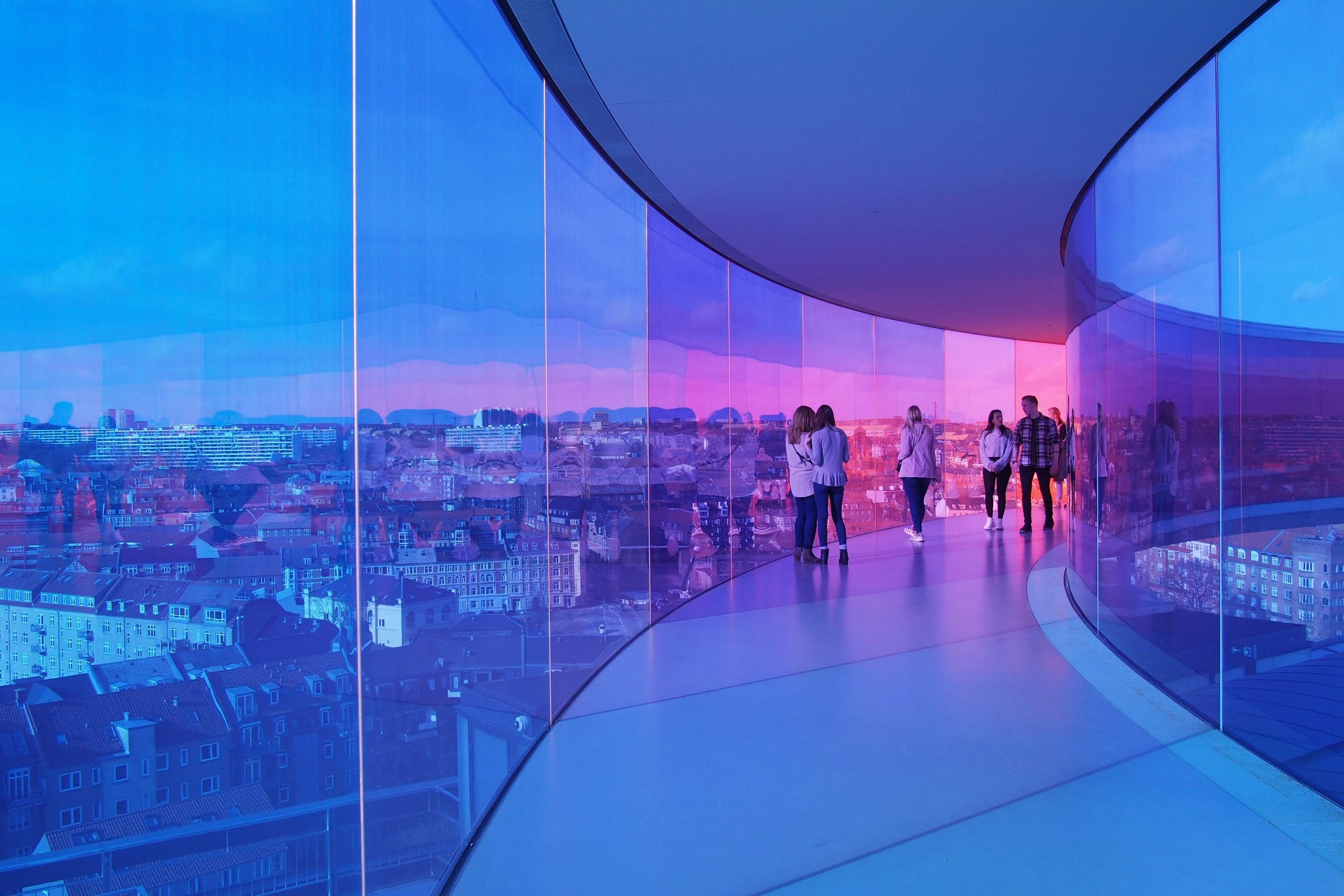 People walking through glass tunnel under clear blue sky.